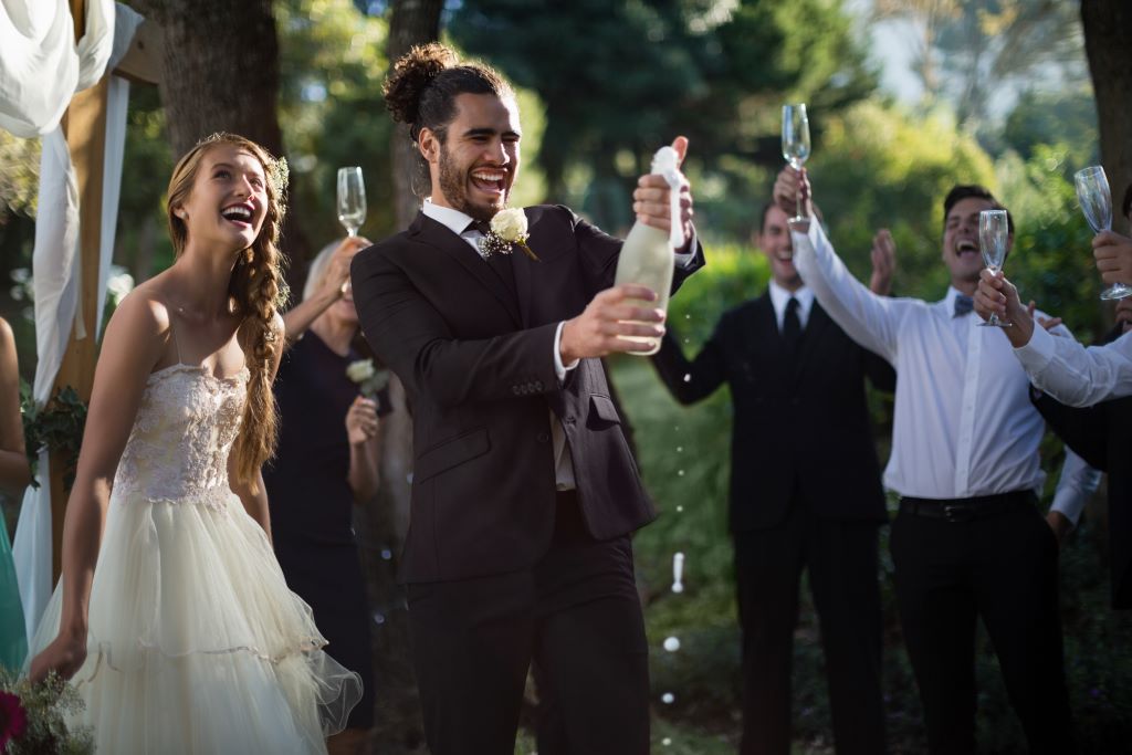 Groom opening champagne bottle at the end of a wedding ceremony
